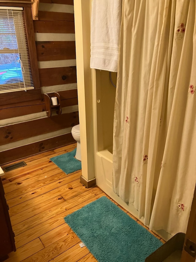 bathroom featuring wood-type flooring, toilet, and shower / bathtub combination with curtain