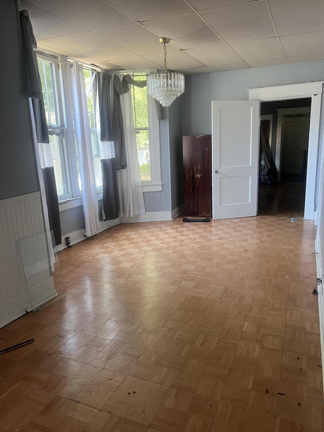 spare room with a wealth of natural light, light parquet flooring, and an inviting chandelier