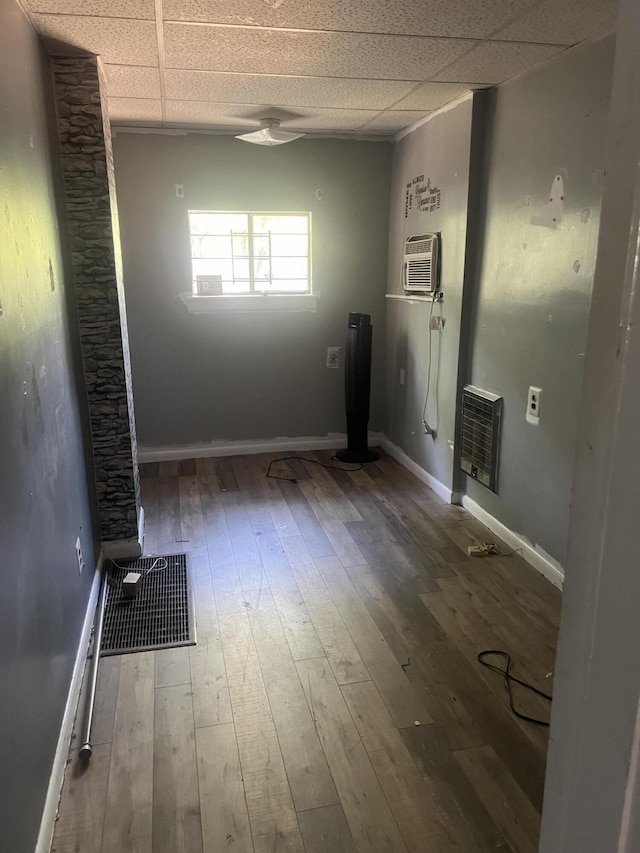 unfurnished room featuring a paneled ceiling, a wall mounted air conditioner, wood-type flooring, and heating unit