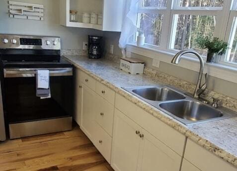 kitchen with white cabinetry, electric range, sink, light stone counters, and light hardwood / wood-style flooring