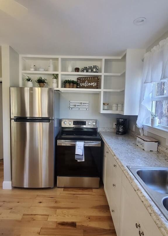 kitchen with sink, light stone counters, light hardwood / wood-style floors, white cabinets, and appliances with stainless steel finishes