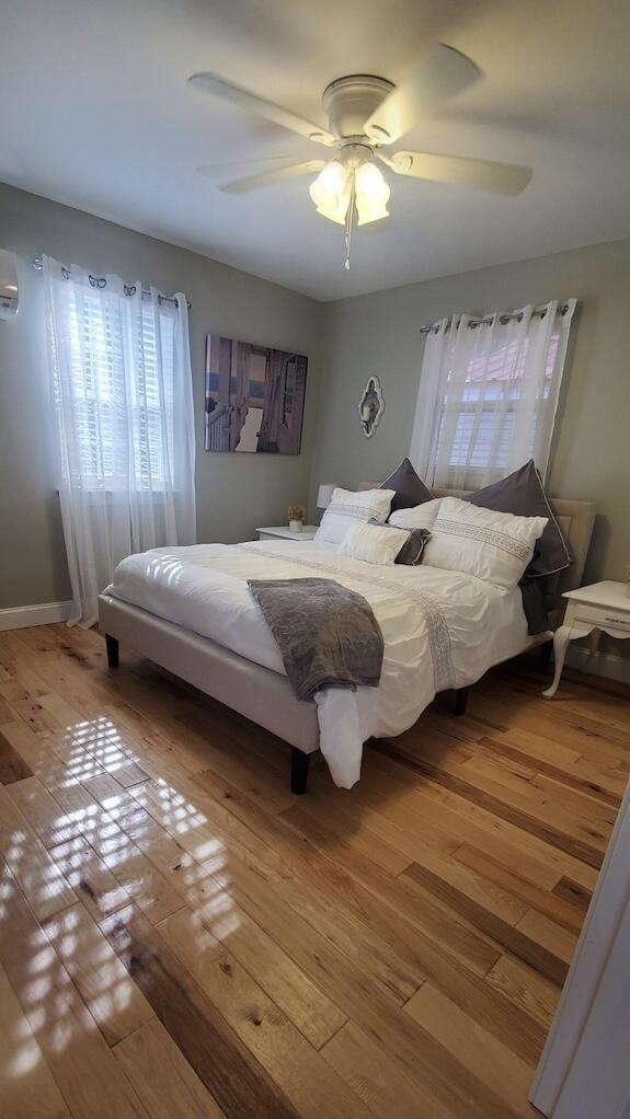 bedroom with a wall mounted air conditioner, light wood-type flooring, and ceiling fan