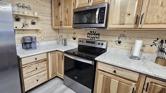 kitchen with stainless steel appliances, light stone counters, light hardwood / wood-style flooring, wood walls, and light brown cabinetry