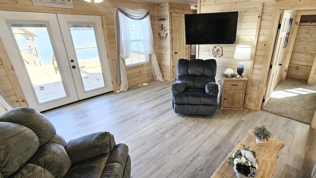 living room featuring wooden walls, french doors, and light hardwood / wood-style floors