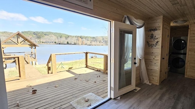 doorway to outside featuring dark hardwood / wood-style flooring, wooden walls, a water view, wooden ceiling, and stacked washer and dryer