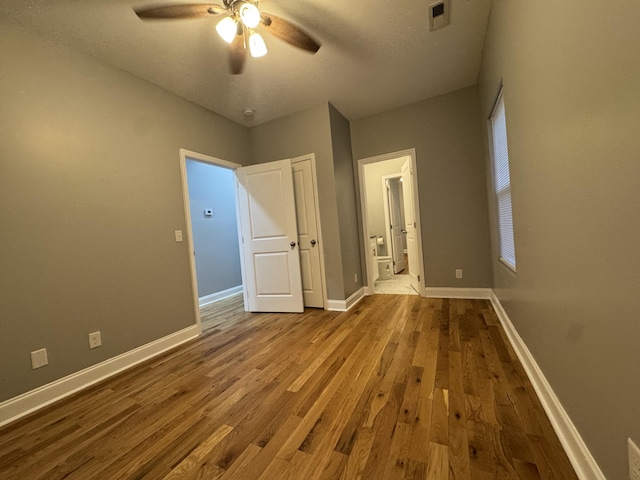 unfurnished bedroom with a textured ceiling, connected bathroom, light hardwood / wood-style floors, and ceiling fan