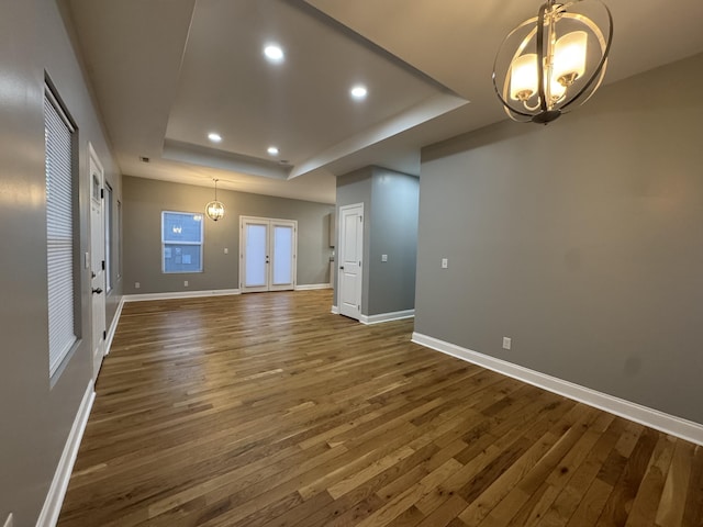 unfurnished living room with a tray ceiling, dark hardwood / wood-style flooring, a chandelier, and french doors