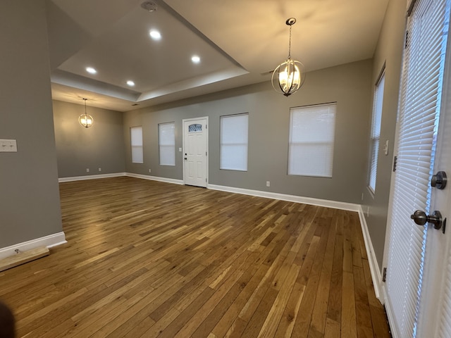 foyer with a raised ceiling, wood-type flooring, and an inviting chandelier