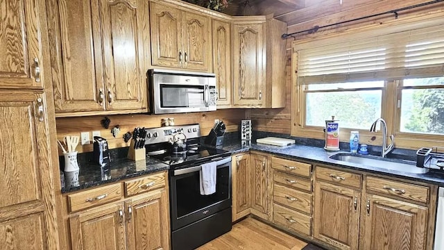 kitchen with dark stone countertops, light wood-type flooring, sink, and appliances with stainless steel finishes