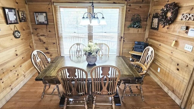 dining room with wood walls, a notable chandelier, and hardwood / wood-style flooring