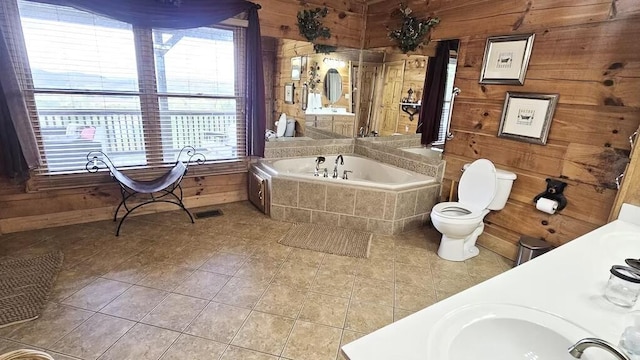 bathroom with tile patterned floors, tiled bath, wood walls, toilet, and vanity