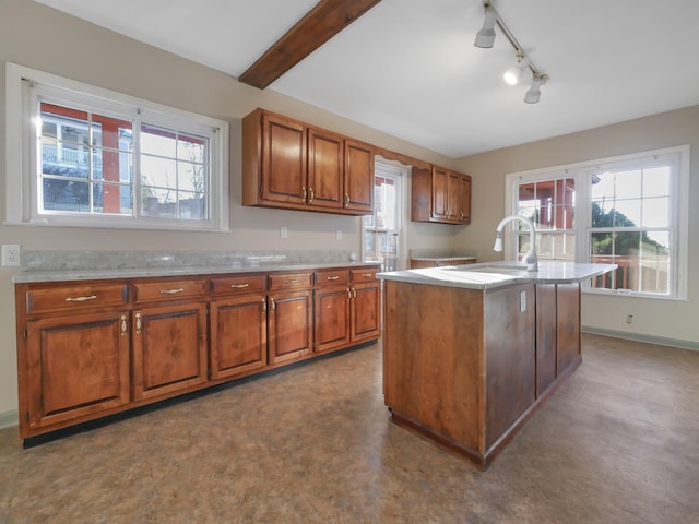 kitchen with beamed ceiling, sink, track lighting, and an island with sink