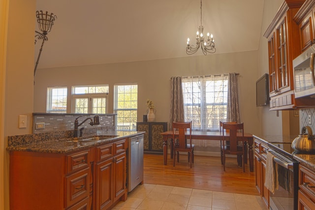 kitchen with sink, stainless steel appliances, a notable chandelier, dark stone counters, and light tile patterned flooring