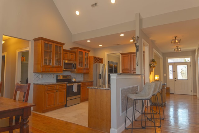 kitchen featuring appliances with stainless steel finishes, light wood-type flooring, tasteful backsplash, light stone counters, and high vaulted ceiling