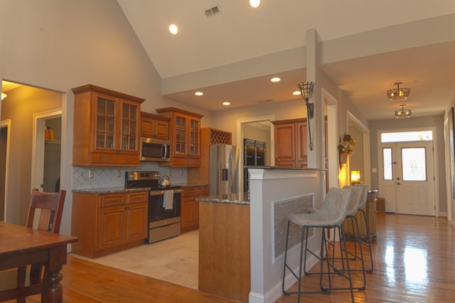 kitchen with stone counters, tasteful backsplash, light hardwood / wood-style flooring, high vaulted ceiling, and appliances with stainless steel finishes