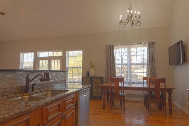 kitchen featuring dishwasher, dark stone counters, an inviting chandelier, sink, and light hardwood / wood-style floors