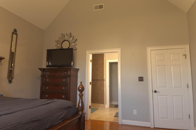 bedroom with connected bathroom, vaulted ceiling, and light wood-type flooring