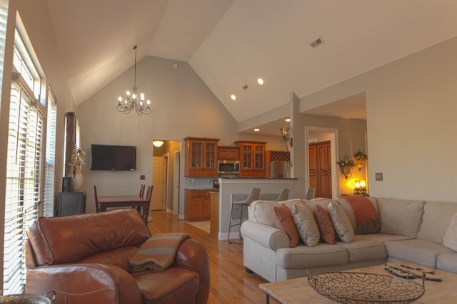 living room with light hardwood / wood-style flooring, high vaulted ceiling, and an inviting chandelier