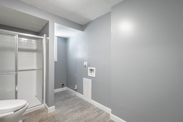 bathroom featuring hardwood / wood-style floors, toilet, a shower with door, and a textured ceiling