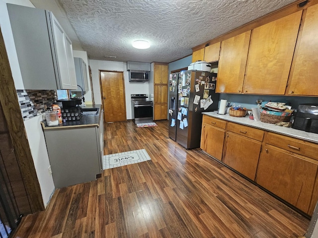 kitchen with a textured ceiling, tasteful backsplash, stainless steel appliances, and dark wood-type flooring