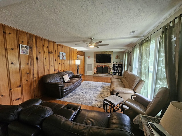 living room with wood-type flooring, a textured ceiling, ceiling fan, and wooden walls