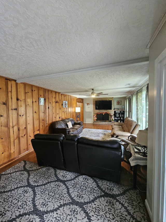 living room featuring a textured ceiling, ceiling fan, ornamental molding, and wood walls