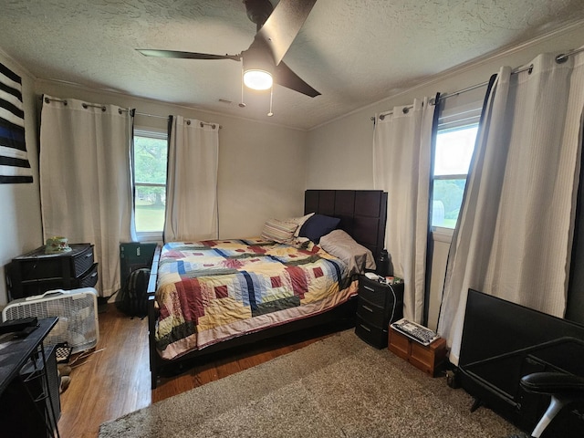 bedroom featuring ceiling fan, wood-type flooring, a textured ceiling, and ornamental molding