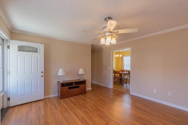 empty room featuring ceiling fan with notable chandelier, light wood-type flooring, ornamental molding, and a textured ceiling