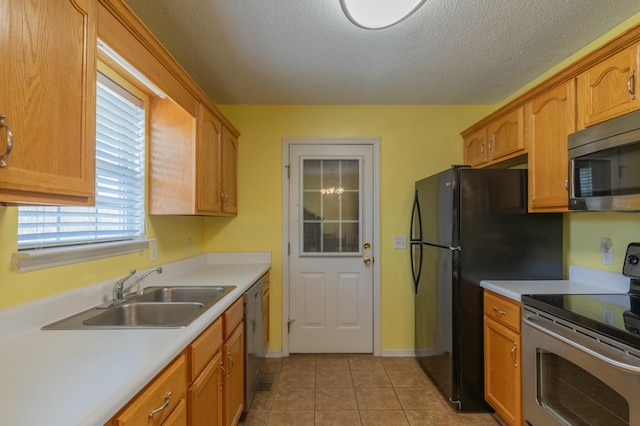 kitchen with sink, stainless steel appliances, light tile patterned flooring, and a textured ceiling