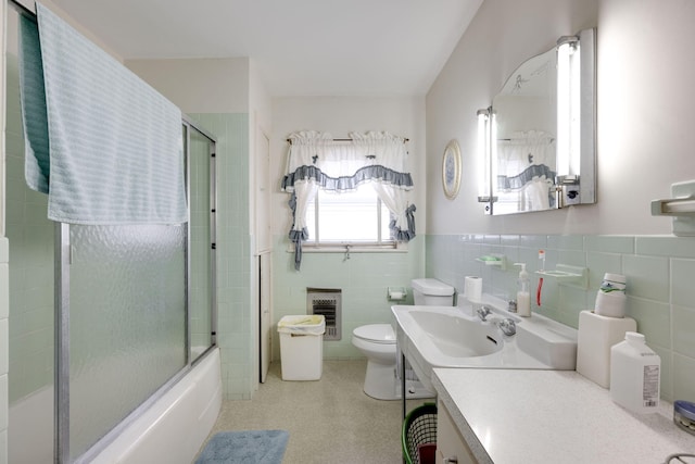 full bathroom with combined bath / shower with glass door, vanity, heating unit, tile walls, and toilet