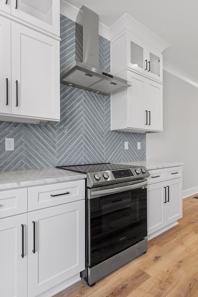 kitchen featuring electric stove, wall chimney exhaust hood, decorative backsplash, light hardwood / wood-style floors, and white cabinetry