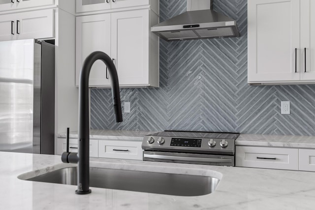 kitchen featuring light stone countertops, white cabinets, stainless steel appliances, and wall chimney range hood