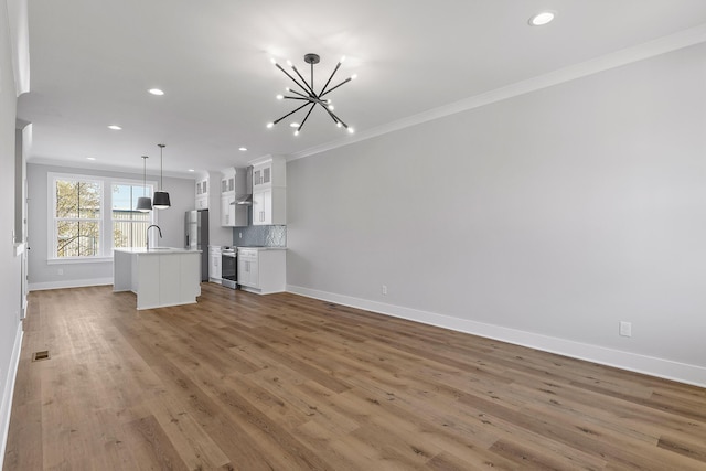 unfurnished living room featuring an inviting chandelier, ornamental molding, sink, and dark wood-type flooring