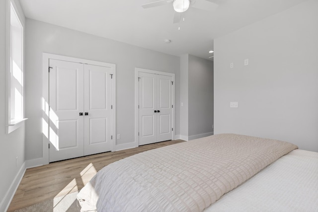 bedroom with light wood-type flooring, ceiling fan, and multiple closets