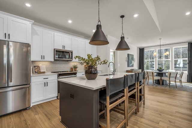 kitchen with pendant lighting, a center island with sink, sink, appliances with stainless steel finishes, and white cabinetry