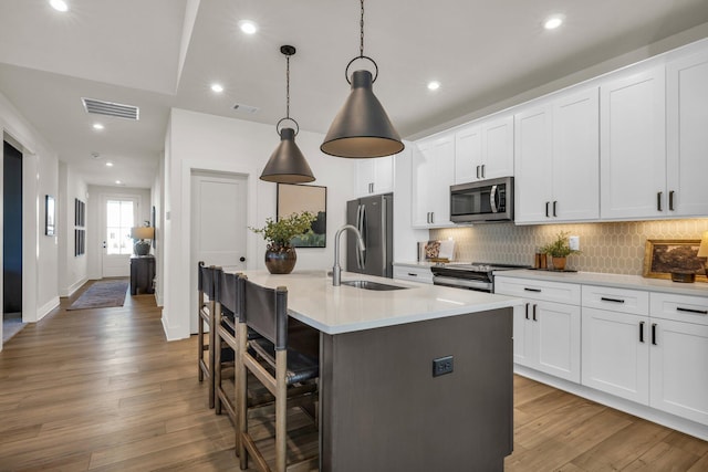 kitchen featuring a kitchen breakfast bar, hanging light fixtures, an island with sink, and stainless steel appliances