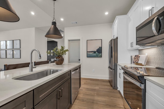 kitchen featuring sink, hanging light fixtures, decorative backsplash, white cabinets, and appliances with stainless steel finishes