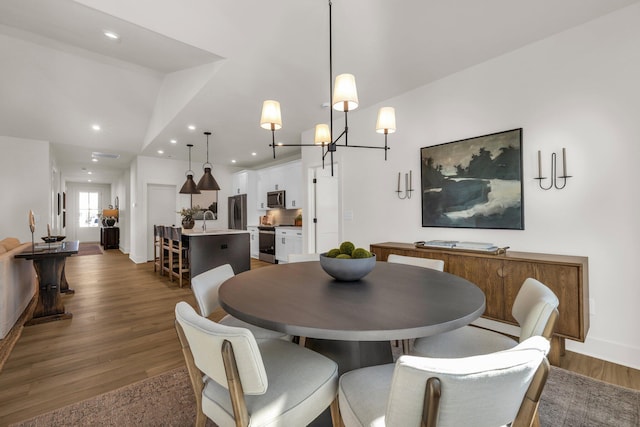 dining room with a chandelier, dark hardwood / wood-style flooring, vaulted ceiling, and sink