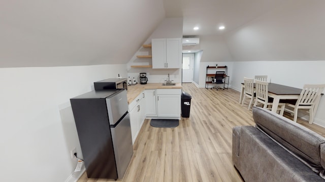 kitchen with white cabinets, a wall mounted air conditioner, sink, and light hardwood / wood-style flooring