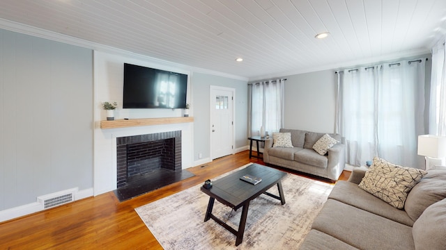 living room with hardwood / wood-style flooring, ornamental molding, wooden ceiling, and a brick fireplace