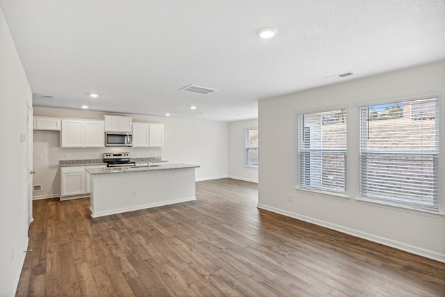 kitchen with dark wood-type flooring, stainless steel appliances, an island with sink, and white cabinets