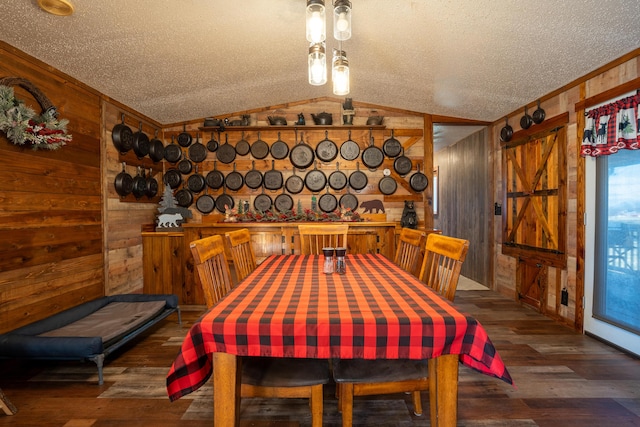 dining room with wood walls, lofted ceiling, a barn door, a textured ceiling, and dark hardwood / wood-style flooring