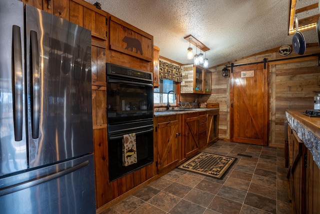 kitchen with a barn door, stainless steel refrigerator, hanging light fixtures, and wooden walls