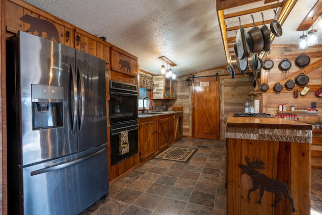 kitchen featuring a barn door, wooden walls, a textured ceiling, and appliances with stainless steel finishes