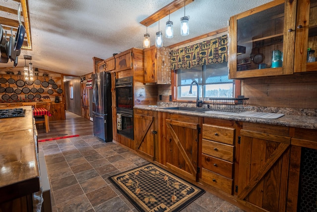 kitchen with pendant lighting, sink, vaulted ceiling, a textured ceiling, and appliances with stainless steel finishes