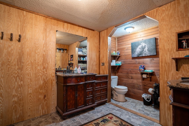 bathroom with vanity, toilet, a textured ceiling, and wooden walls