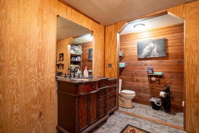 bathroom with wood walls, vanity, a textured ceiling, and toilet