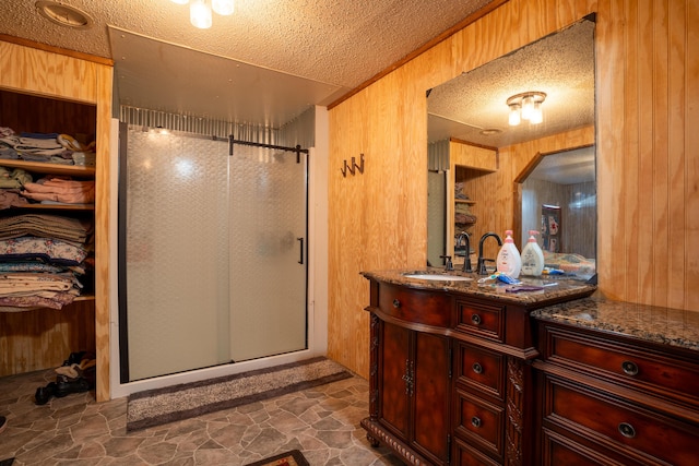 bathroom with a textured ceiling, wood walls, vanity, and an enclosed shower