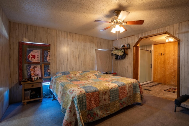 carpeted bedroom with wooden walls, ceiling fan, and a textured ceiling