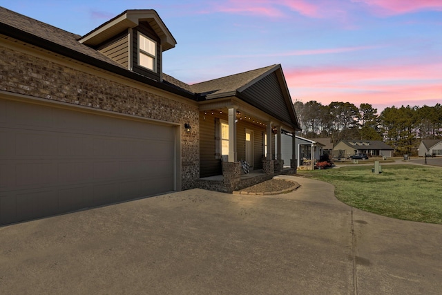 view of property exterior featuring a garage, covered porch, brick siding, driveway, and a lawn